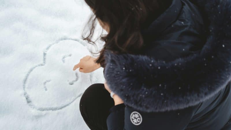 femme dessinant un cœur souriant dans la neige